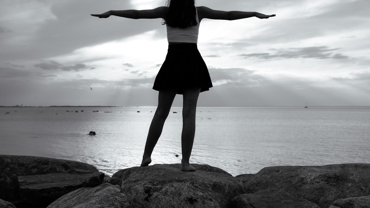A young dark-haired woman in a short black skirt and a white sleeveless crop top standing on large rocks by Tallinn Bay on a summer day. 📸 Photo by me IG: @margoevardson